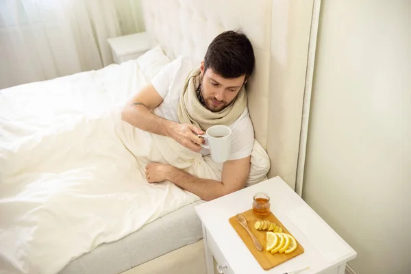 Ο άρρωστος άνθρωπος πίνει ζεστό τσάι στο κρεβάτι στο σπίτι. III Ο άνθρωπος στο σπίτι αυτοθεραπεία. — Φωτογραφία Αρχείου