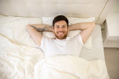 Yatakta Sırıtarak Yatan Yakışıklı Adam. Evde sabahlar. Yukarı, aşağı, ateş. Yatakta Erkek Portresi Kamerada İzleme.