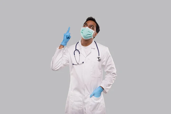 Doctor Pointing Up och Watching Up Wearing Medical Mask och handskar isolerade. Indisk man doktor Bra idé. — Stockfoto