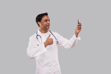 Doktor 'un telefonunda kablosuz kulaklıkla başparmağı yukarı gösteren bir video görüşmesi var. Hintli Adam Doktor Video Çağrısı. Medicine Online. Doktor Telefonu Kullanıyor.
