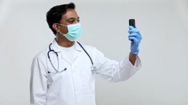 Doktorun telefonunda tıbbi maske ve eldivenlerle görüntülü görüşme yapması izole edildi. Hintli Adam Doktor Video Çağrısı. Medicine Online. Doktor Telefonu Kullanıyor.