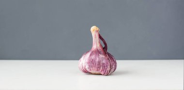 Mor renkli organik sarımsak başı koyu gri arka planda beyaz bir masada.