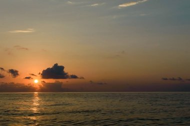 Sakin deniz, parlak günbatımı gökyüzü ve bulutlar arasında güneş. Deniz manzarası üzerinde sarı güneş. Sakin bulutlu gökyüzü ve okyanus yüzeyinin arka planı.