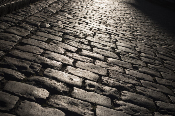 Black cobbled stone road background with reflection of light seen on the road. Black or dark grey stone pavement texture. light on the stone pavement