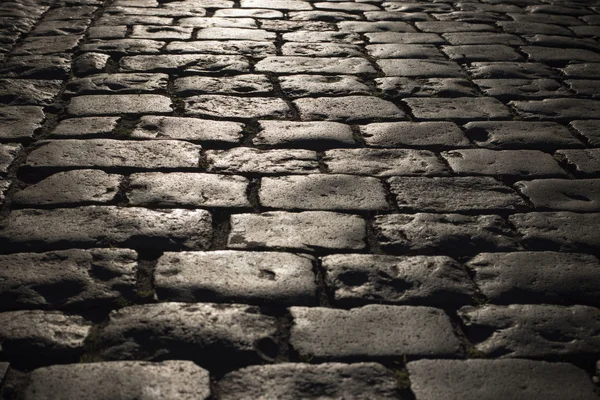 Black cobbled stone road background with reflection of light seen on the road. Black or dark grey stone pavement texture.