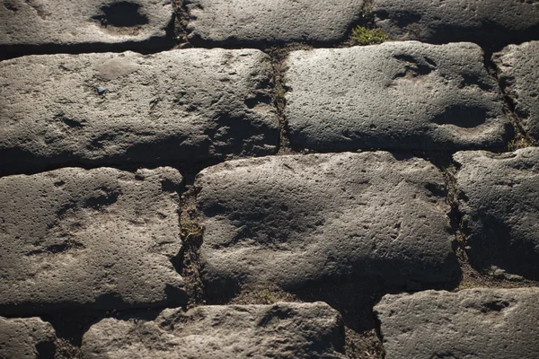 Black cobbled stone road background with reflection of light seen on the road. Black or dark grey stone pavement texture.