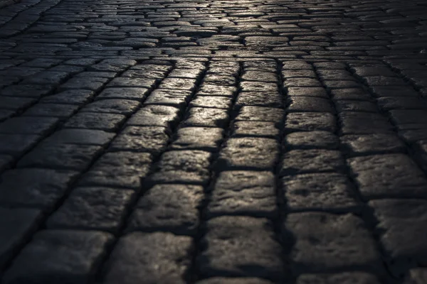 Zwarte geplaveide stenen weg achtergrond met weerkaatsing van het licht gezien op de weg. Zwart of donker grijs natuursteen bestrating textuur. — Stockfoto