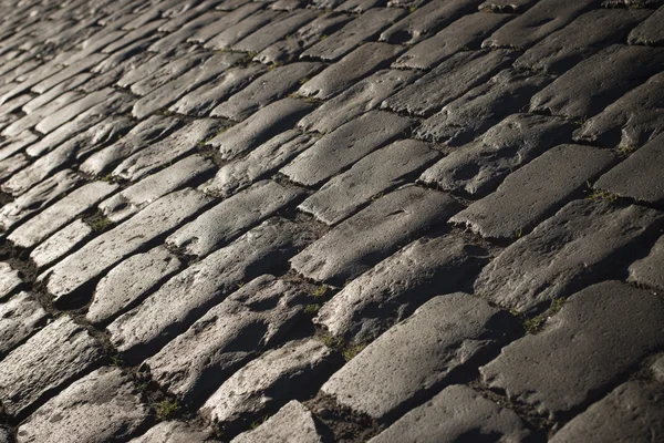 Zwarte geplaveide stenen weg achtergrond met weerkaatsing van het licht gezien op de weg. Zwart of donker grijs natuursteen bestrating textuur. — Stockfoto