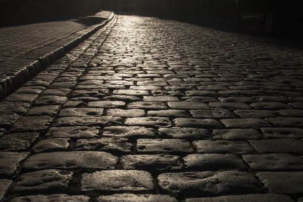 Black cobbled stone road background with reflection of light seen on the road. Black or dark grey stone pavement texture. — Stock Photo, Image