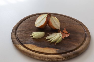 Soğanlar ikiye bölünmüş, dörde bölünmüş ve dilimlenmiş, soğan kabuğu ahşap bir kesme tahtasının üzerinde.