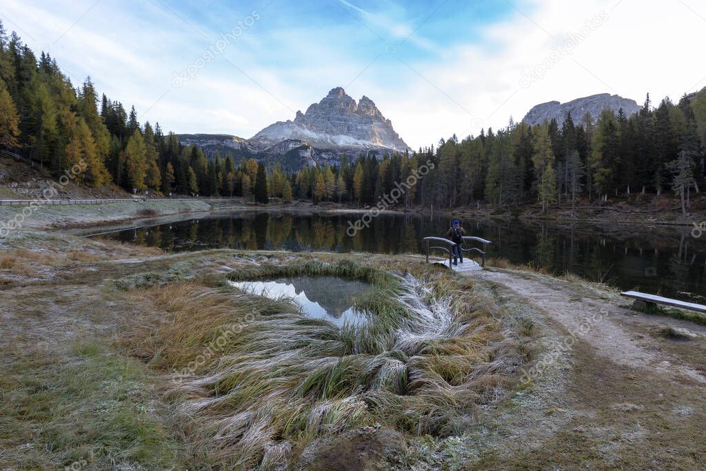 Italian Dolomites, Lago d'Antorno small lake with calm surface in mountains with high spruces. A path and a small wooden bridge lead to the lake. Above the lake the mountain Tre cime.