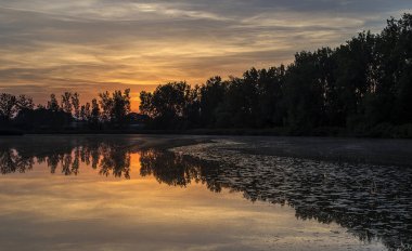Güney Moravya, Dlouhy göletinin üzerinde gün batımı. Arka planda, barajın kenarında, bir sıra ağaç, yaprak döken kavak gölün yüzeyine yansıyor.