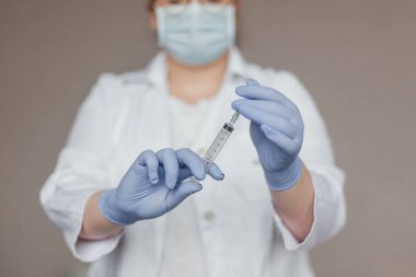 Beyaz önlüklü doktor elinde koronovirüs aşısı olan bir şırınga tutuyor.