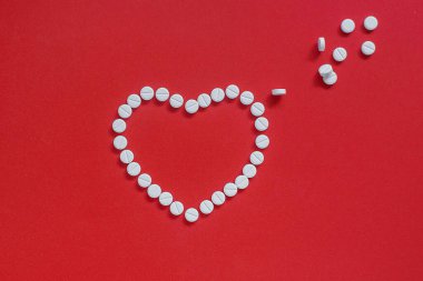 Kırmızı arka planda beyaz haplardan yapılmış kalp.