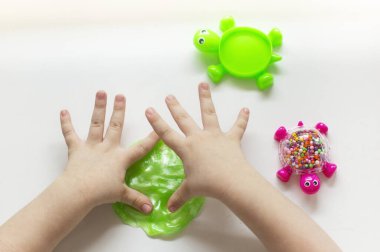 Çocuk elinde yeşil balçık oynuyor, şeffaf oyuncak. Küçük çocuk yeşil sümükle oynuyor.