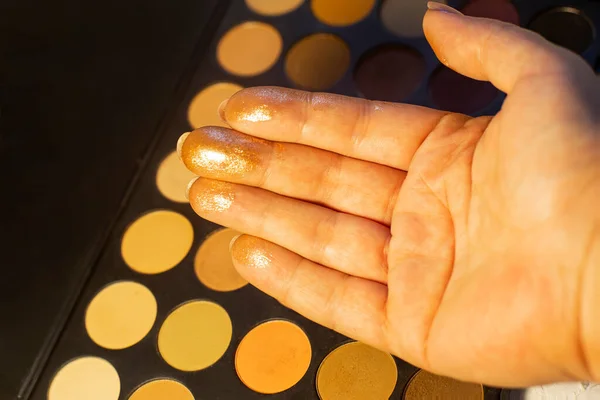 Eye shadow swatches on woman hand. Hand with golden shadows on a background of eye shadow palette. Black background