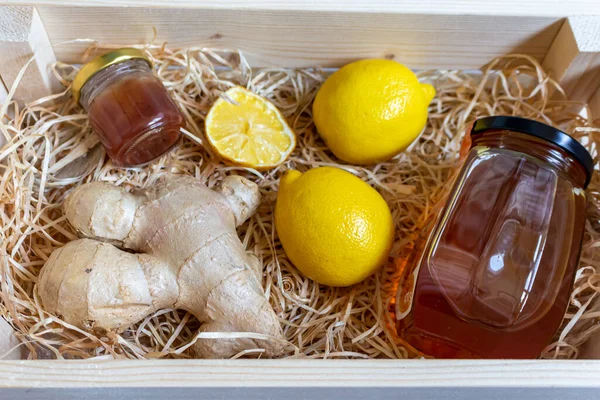 A wooden box with medicines for the virus and coronavirus, in which there are two ripe lemons, half a lemon, a jar of honey, ginger root and a jar of jam. Vitamins for health.