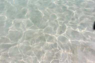 parlak şeffaf temiz su yüzeyi güneşte parıldıyor ve okyanusun dibindeki ve denizdeki hafif kumların arka planında.