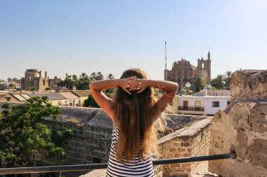 Ayia NAPA / Cyprus - 09.13.2018: Kıbrıs 'ta tatilde boyasız uzun saçlı güzel bir turist kız uzun bir elbise giymiş ve antik kentin manzarasına bakıyor.