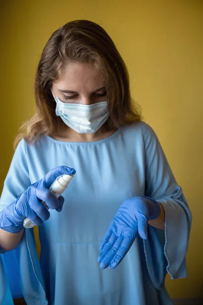 a young woman wearing a protective medical mask and gloves sprays her hands with antiseptic to avoid catching the coronavirus virus and kill germs
