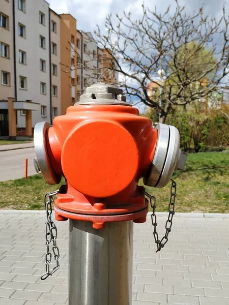 red fire hydrant in the city with chains on the background of a well-groomed entrance in summer