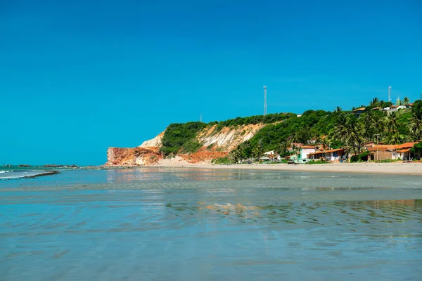 Sunny morning, where you can see boats, houses and the cliff with vegetation in the background in Praia Redonda, Icapui, Ceara, Brazil on April 23, 2016