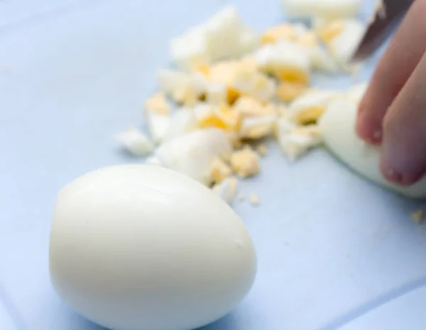 Cortando o ovo de salada em uma placa de corte azul. ao lado de todo o ovo cozido . — Fotografia de Stock