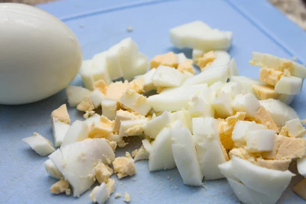 Diced boiled egg to cook on a blue cutting board. — Stock Photo, Image