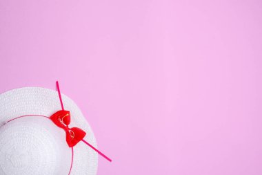 Sol alt köşedeki pembe arka planda kırmızı kurdeleli beyaz bir kadın şapkası yatıyor.