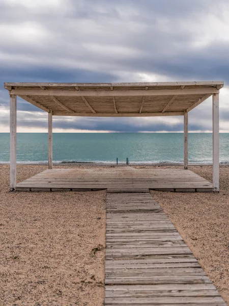 wooden walkway and sunshades on sand beach with azure sea, cloudy sky background. Empty beach with sunshades. Evpatoriya, Crimea. Copy space. The concept of calmness, silence and unity with nature
