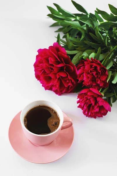 pink cup of coffee and three red peonies on the white background