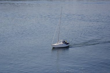 Baltık Denizi. 25 Temmuz 2014. Küçük beyaz yelkenli Stockholm körfezinde yelken açıyor. Sırtında İsveç bayrağı dalgaları.