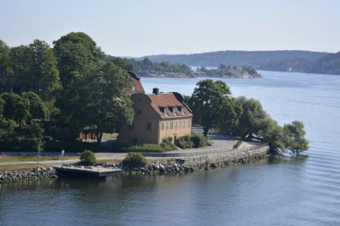 Baltık Denizi, İsveç kıyısı. 25 Temmuz 2014. Su kenarında kırmızı çatılı geleneksel bir İskandinav evi. Etrafında bereketli bitkiler olan güzel bir park..