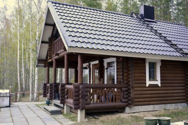 Güney Karelya, Finlandiya, 10 Mayıs, 201. Teraslı ahşap kahverengi ev, yeşil bahar ormanlarında gri kiremitli çatı..