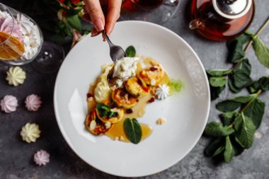 Dişi eller çatal ve bıçakla krep tutuyor. Cheesecake, taze reçel ve nane. Süzme peynirli krep ya da kremalı börek tabağa yakın duran pudra şekerli..