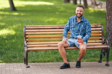 Limonatalı bir adam baharda bir bankta dinleniyor. Güneşli bir gün. Yeşil yaprak.