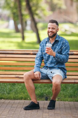 Limonatalı bir adam baharda bir bankta dinleniyor. Güneşli bir gün. Yeşil yaprak.