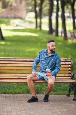 Limonatalı bir adam baharda bir bankta dinleniyor. Güneşli bir gün. Yeşil yaprak.