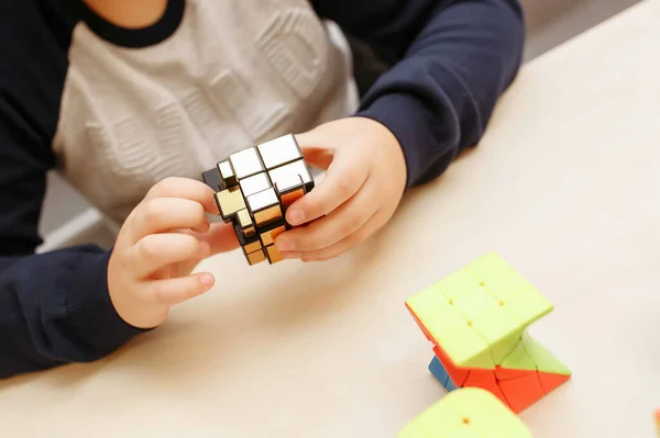 Rubik\'s cube in children\'s hands, closeup, white wooden background. Boy holding Rubik\'s cube and playing with it.