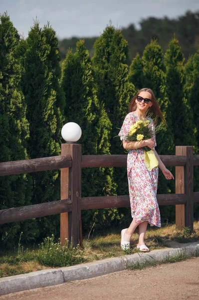 Stilvolles Mädchen posiert in einem Kleid in einem sonnigen Frühlingspark. Ruhiges Porträt eines schönen Mädchens, das mit einem Strauß im Frühling steht — Stockfoto