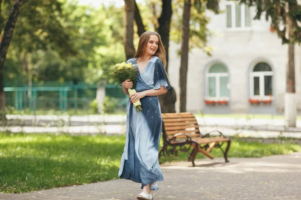 Stilvolles Mädchen posiert in einem Kleid in einem sonnigen Frühlingspark. Ruhiges Porträt eines schönen Mädchens, das mit einem Strauß im Frühling steht — Stockfoto
