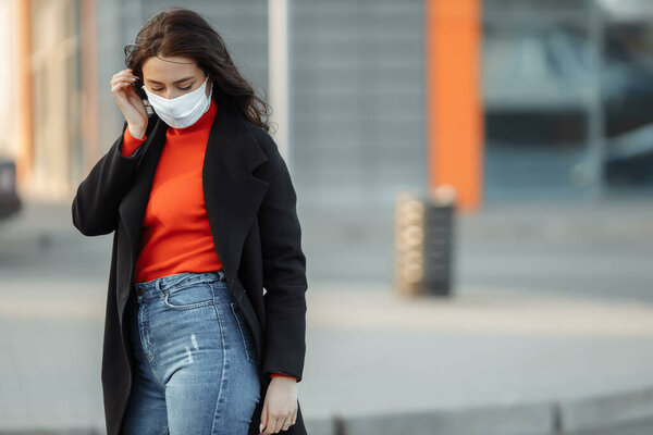 Portrait of beautiful woman walking on the street wearing protective mask as protection against infectious diseases. Attractive unhappy model with flu outdoors