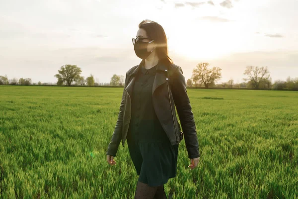 Une fille portant un masque médical court ou marche sur un champ vert. Quarantaine printemps été. coronavirus. COVID 19. Virus de la grippe, rhume — Photo