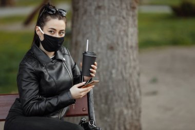 Siyah koruyucu maskeli esmer bir kadının portresi bankta oturuyor.