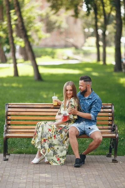 Moda casal adolescente descansando em um parque da cidade com bebidas sentadas em um banco — Fotografia de Stock