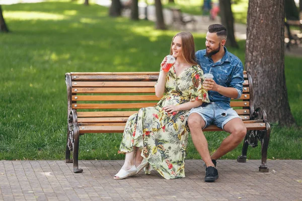 Moda casal adolescente descansando em um parque da cidade com bebidas sentadas em um banco — Fotografia de Stock