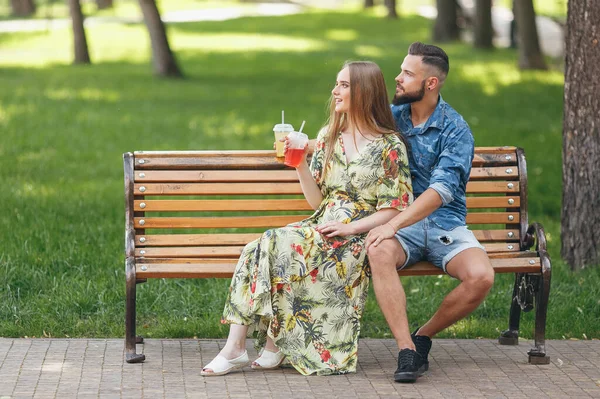 Moda casal adolescente descansando em um parque da cidade com bebidas sentadas em um banco — Fotografia de Stock