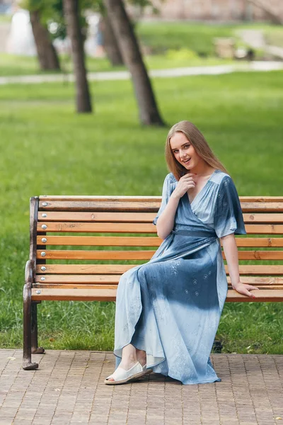 Menina bonita sentada em um banco, morena em um vestido brilhante, dia ensolarado — Fotografia de Stock