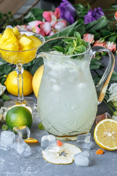 夏の新鮮な冷たい飲み物 テーブルの屋外にミントとジャグとレモンとオレンジで氷のレモネード ジャグの中のオレンジレモネード — ストック写真