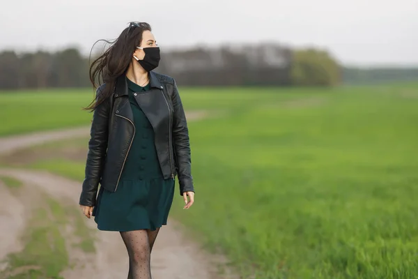 girl in a medical mask runs or walks on a green field Quarantine spring summer